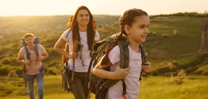 Eine junge Familie geht im Sonnenschein wandern. Die junge Tochter steht im Vordergrund.