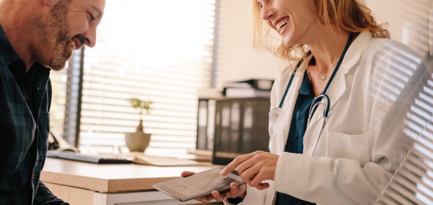 Eine Ärztin berät einen männlichen Patienten und hält ein Tablet in der Hand.