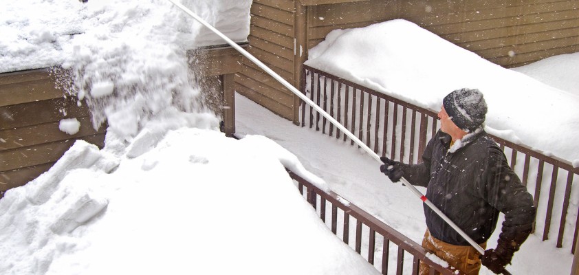 Ein Mann mit einem Schnee-Rechen entfernt Schnee vom Dach.