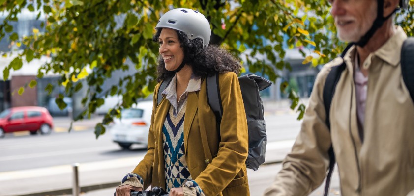 Älterer Mann fährt neben einer jüngeren Frau geschützt mit Helm E-Scooter.