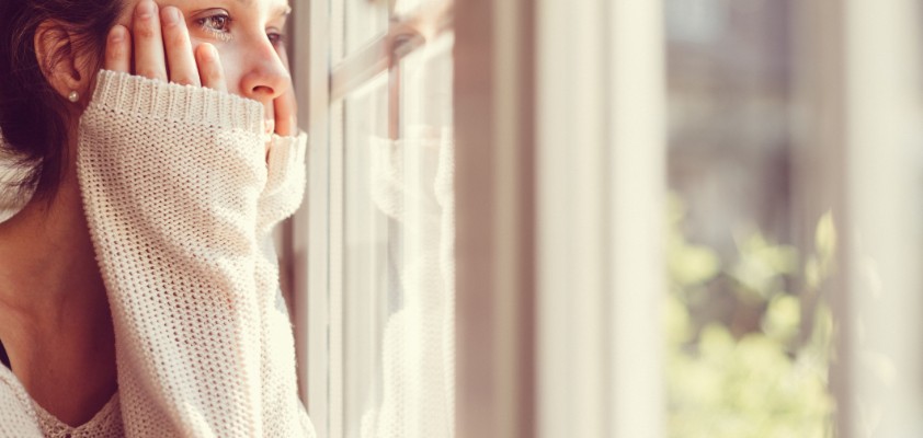 Eine junge Frau schaut aus einem Fenster in die Ferne. 
