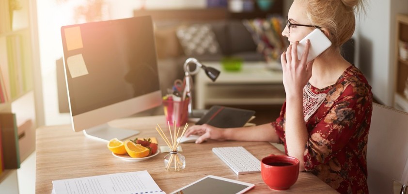 Eine Frau telefoniert, während sie an ihrem Schreibtisch am Laptop arbeitet.
