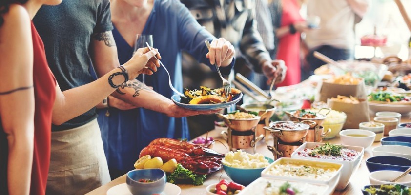 Mehrere Menschen stehen an einem vielseitigen, vollen Buffet.