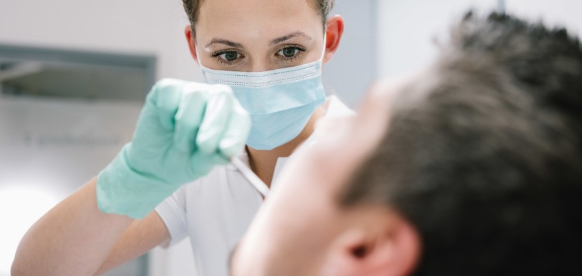 Eine Zahnärztin schaut einem Patienten in den Mund. 