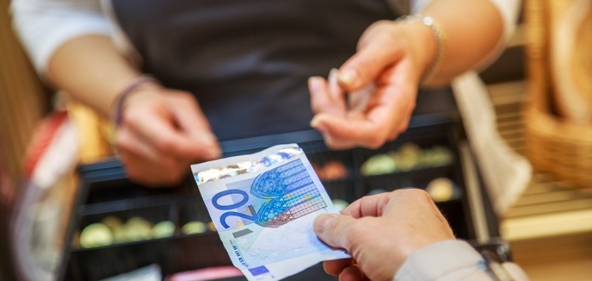 Die Hand einer Frau hält einer Kassiererin einen 20€ Geldschein hin. 