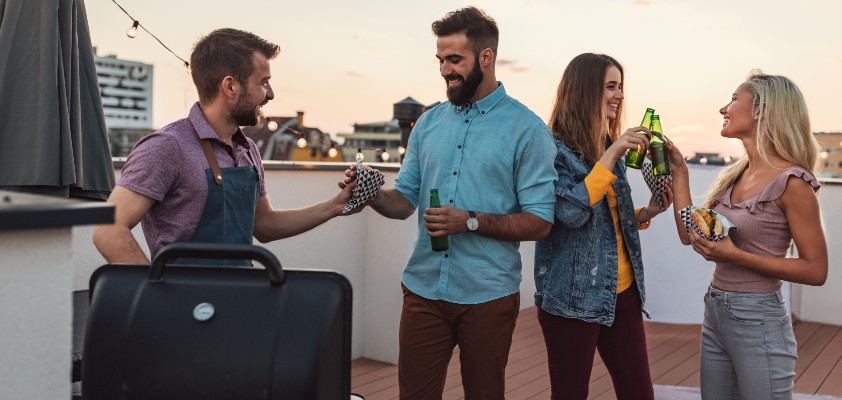 Eine Gruppe von Leuten grillt zusammen auf einer Dachterrasse. 