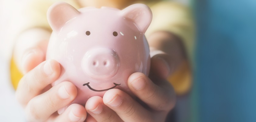 Ein kleines Kind hält ein rosafarbenes Sparschwein in die Kamera. 