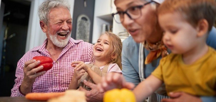 Großeltern kochen lachend gemeinsam mit ihren zwei kleinen Enkelkindern