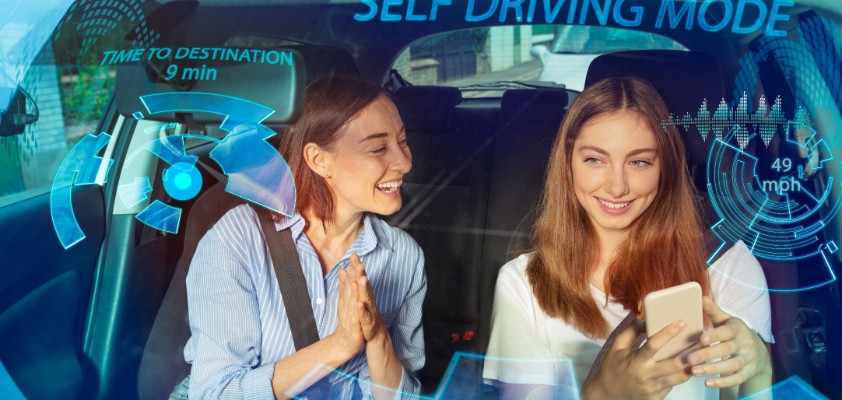 Zwei Freundinnen sitzen zusammen vorne im Auto und schauen in ein Smartphone.