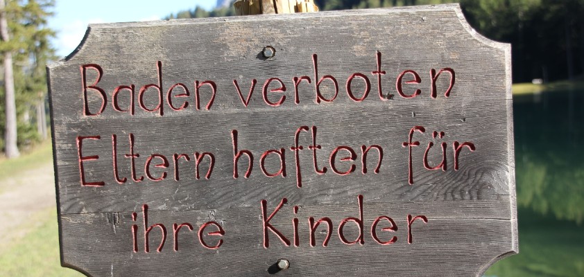 Ein Holzschild an einem See auf dem steht "Baden verboten. Eltern haften für ihre Kinder."