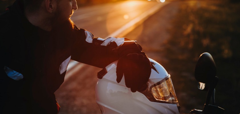 Motorradfahrer macht während einer Fahrt bei Sonnenuntergang eine Pause. Der Helm liegt auf dem Motorrad.