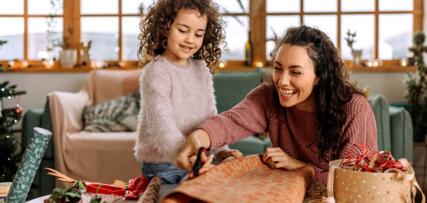 Eine Mutter packt mit ihrer kleinen Tochter Weihnachtsgeschenke ein. 