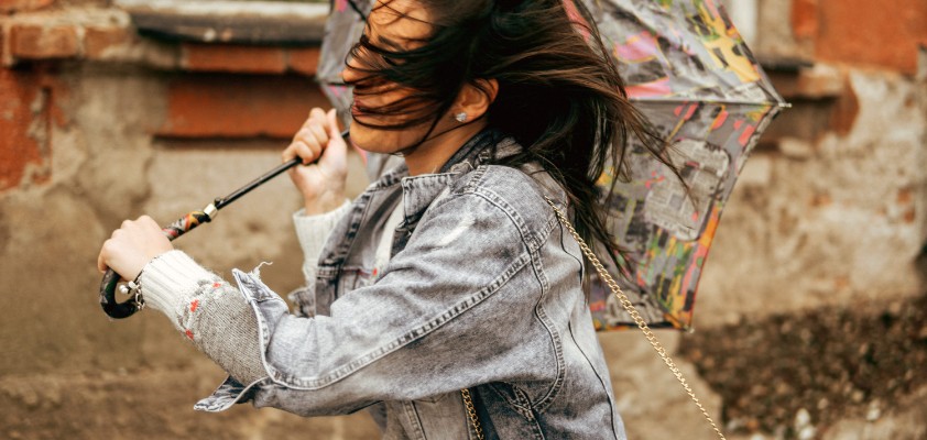 Eine Frau läuft mit ihrem Regenschirm durch einen starken Wind. Der Regenschirm hat sich bereits umgedreht. 