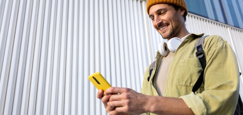 Ein junger Mann schaut beim Gehen lächelnd auf sein Handy