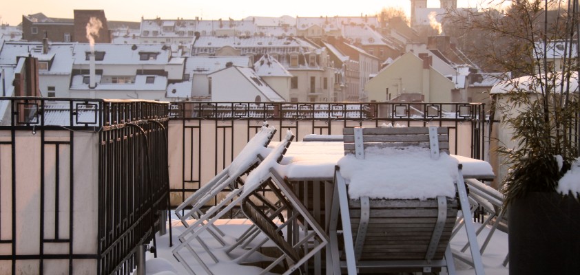 Das Bild zeigt einen Balkon mit Möbeln, die verschneit sind. 