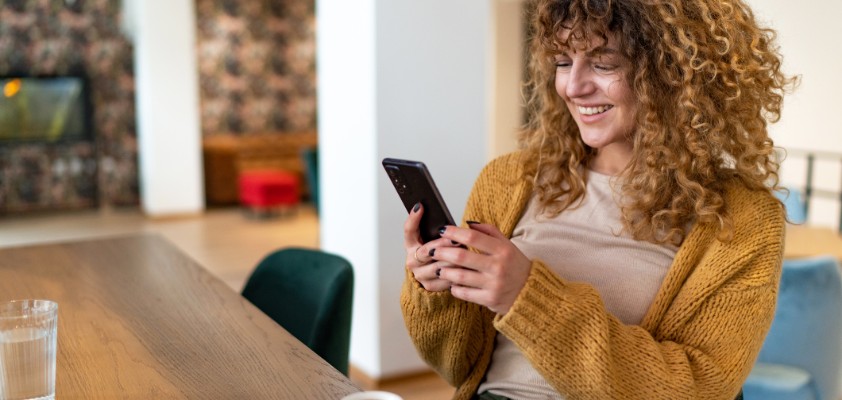 Person sitzt in einem Café und benutzt ein Smartphone, mit einer Tasse Kaffee auf dem Tisch.
