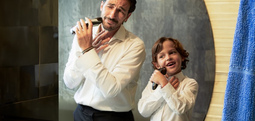 Vater und sein Sohn im Kindesalter stehen im Hemd vor einem Spiegel und rasieren sich im Gesicht