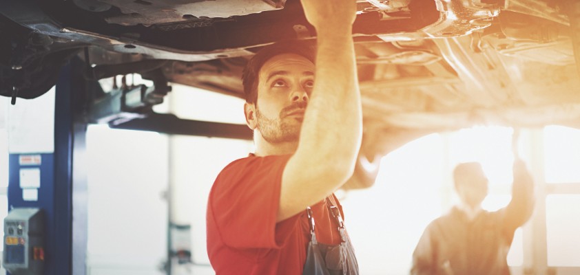 Ein Mann arbeitet am unteren Teil eines hochgefahrenen Autos in einer Werkstatt 