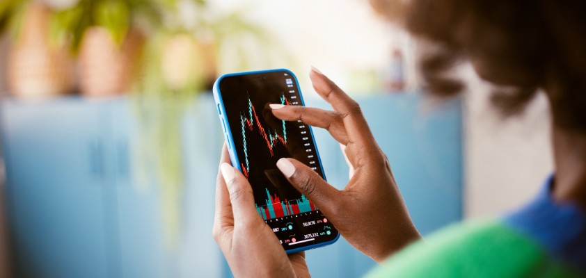 Frau zoomt mit den Fingern näher an eine Aktien-Grafik auf ihrem Handy.