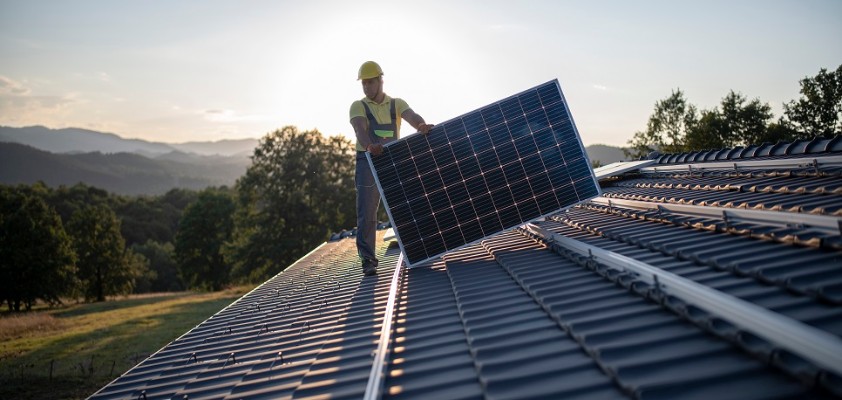 Ein Mann verlegt auf dem Dach eines Hauses Solarpanels.