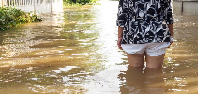 Eine Frau steht bis zu den Oberschenkeln im Wasser einer überschwemmten Straße.