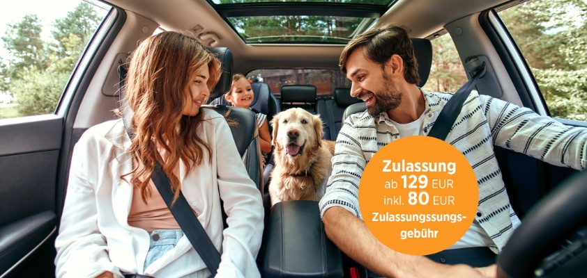 Eine junge Familie, fotografiert aus der Perspektive des Autocockpits, sitzt angeschnallt Auto und haben ihren goldbeigen Hund auf der Rückbank mit dabei.