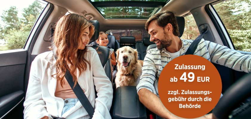 Eine junge Familie, fotografiert aus der Perspektive des Autocockpits, sitzt angeschnallt Auto und haben ihren goldbeigen Hund auf der Rückbank mit dabei.
