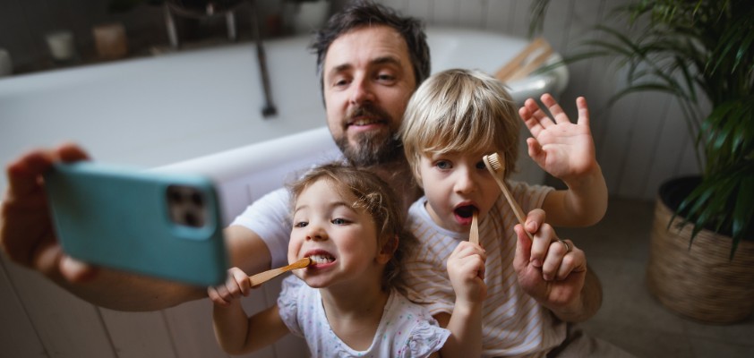 Ein Vater nimmt mit seiner Tochter und seinem Sohn ein Selfie auf, während sie beide am Zähne putzen sind.