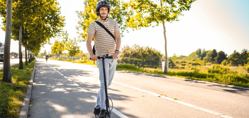 Mann trägt Schutzhelm beim Fahren mit seinem E-Scooter.