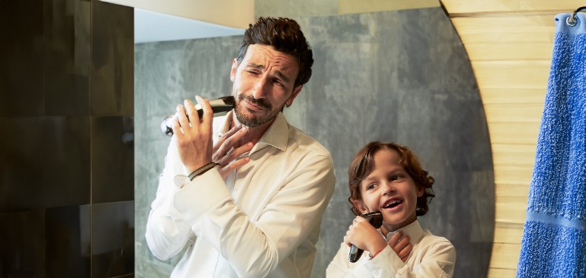 Vater und sein Sohn im Kindesalter stehen im Hemd vor einem Spiegel und rasieren sich im Gesicht