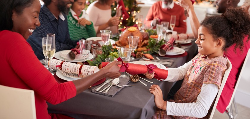 Eine mehrköpfige, dunkelhäutige Familie sitzt zusammen lachend am Weihnachtstisch. 