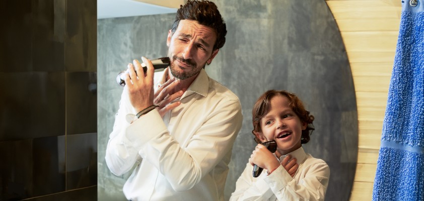 Vater und sein Sohn im Kindesalter stehen im Hemd vor einem Spiegel und rasieren sich im Gesicht