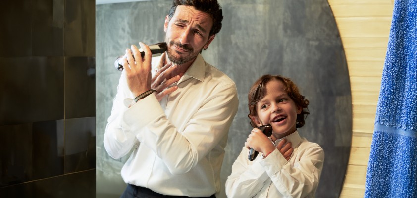 Vater und sein Sohn im Kindesalter stehen im Hemd vor einem Spiegel und rasieren sich im Gesicht