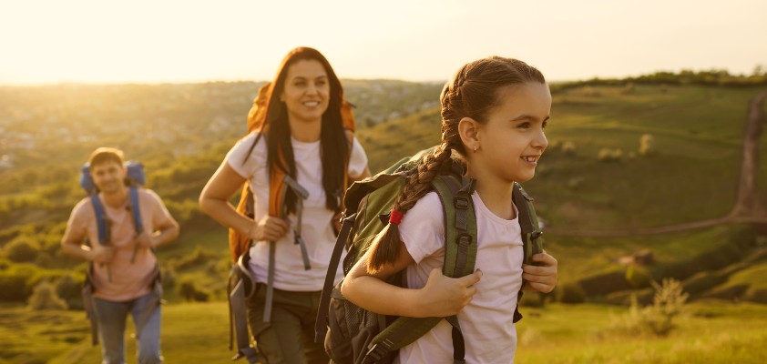 Eine junge Familie geht im Sonnenschein wandern. Die junge Tochter steht im Vordergrund.