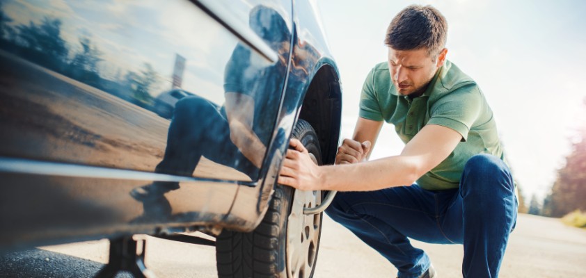 Ein Mann wechselt eigenständig den Reifen seines Autos. 