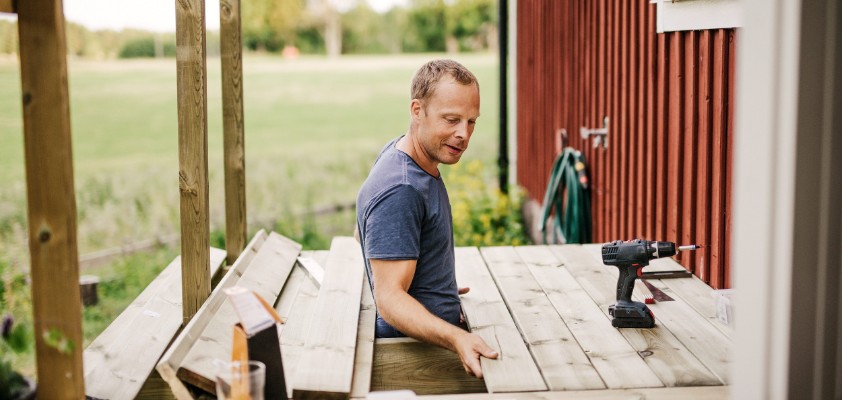 Ein Mann arbeitet an der Holzterrasse eines roten Schwedenhauses. 