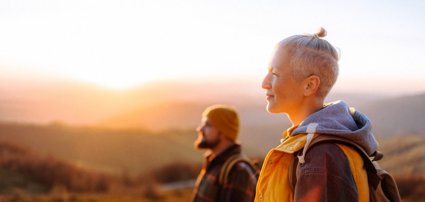 Eine Frau und ein Mann stehen in goldenem Licht in der Landschaft und schauen nach links.