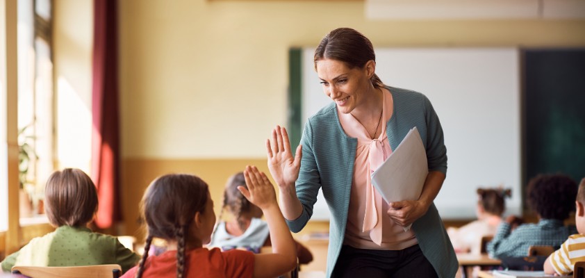Eine Lehrerin läuft durch ihre Klasse und gibt einer Schülerin ein "high five"