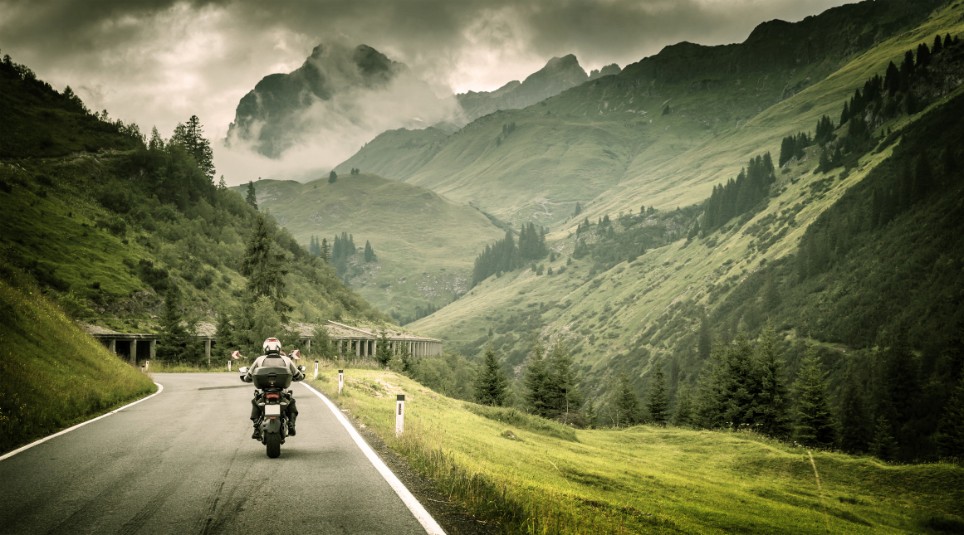 Eine Person fährt mit dem Motorrad auf einer Straße durch eine Berglandschaft Eine Person fährt mit dem Motorrad auf einer Straße durch eine Berglandschaft