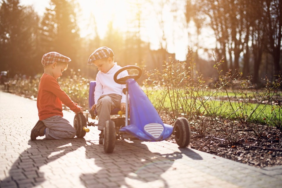 Zwei junge Kinder prüfen gemeinsam den Reifendruck ihres Gokarts Zwei junge Kinder prüfen gemeinsam den Reifendruck ihres Gokarts