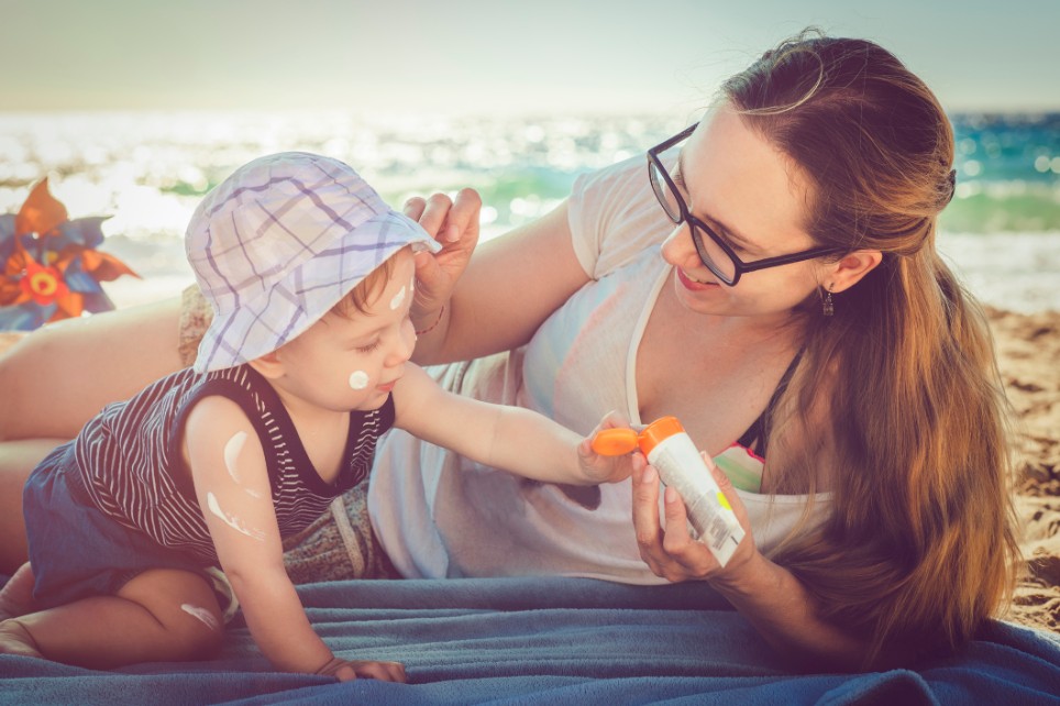 Eine Mutter cremt ihr Kleinkind am Strand mit Sonnencreme ein Eine Mutter cremt ihr Kleinkind am Strand mit Sonnencreme ein