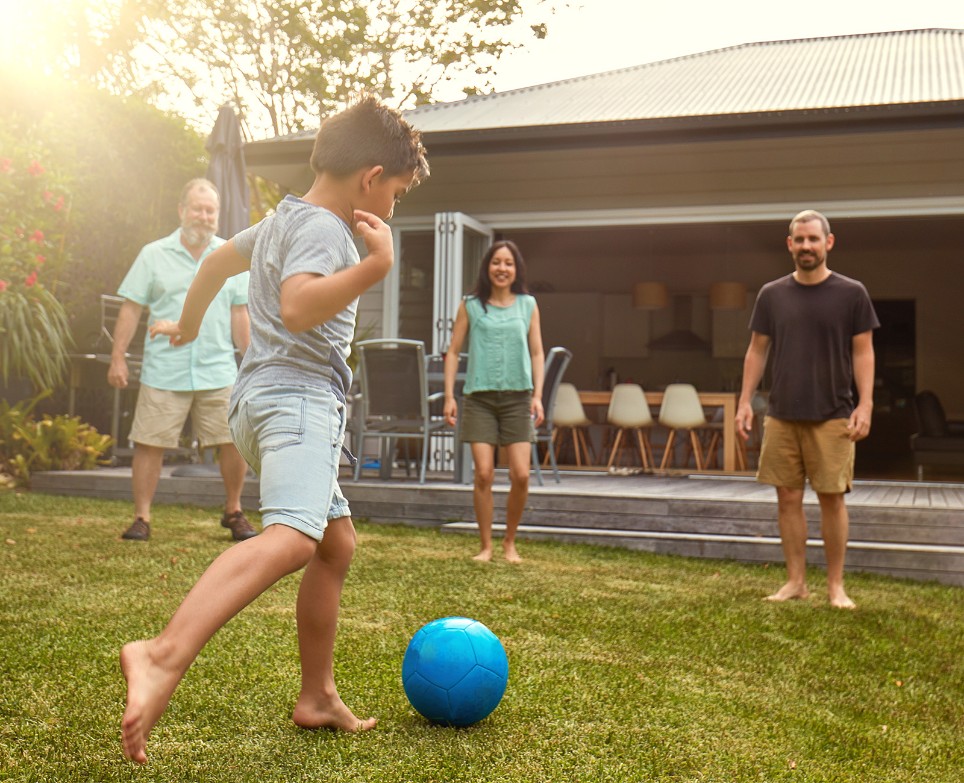 Ein kleiner Junge tritt gegen einen blauen Ball, beobachtet von zwei Männern und einer Frau. Ein kleiner Junge tritt gegen einen blauen Ball, beobachtet von zwei Männern und einer Frau.