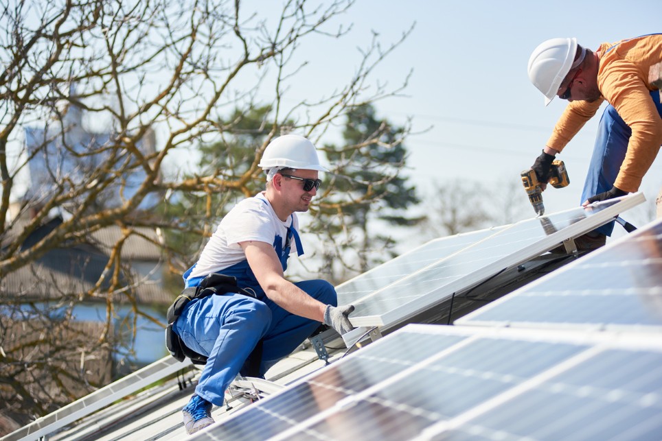Zwei Handwerker montieren eine Solaranlage auf einem Dach Zwei Handwerker montieren eine Solaranlage auf einem Dach