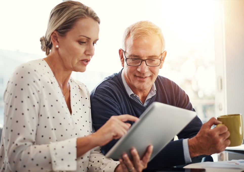 Ein Mann und eine Frau schauen gemeinsam auf ein Tablet und besprechen etwas. 