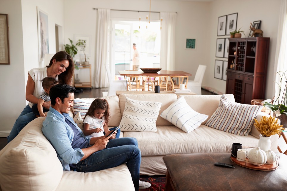 Eine vierköpfige junge Familie sitzt zusammen im Wohnzimmer auf dem Sofa. 