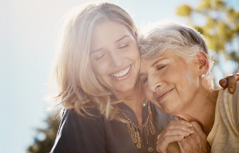 Ältere und jüngere Frau schmiegen sich lächelnd aneinander