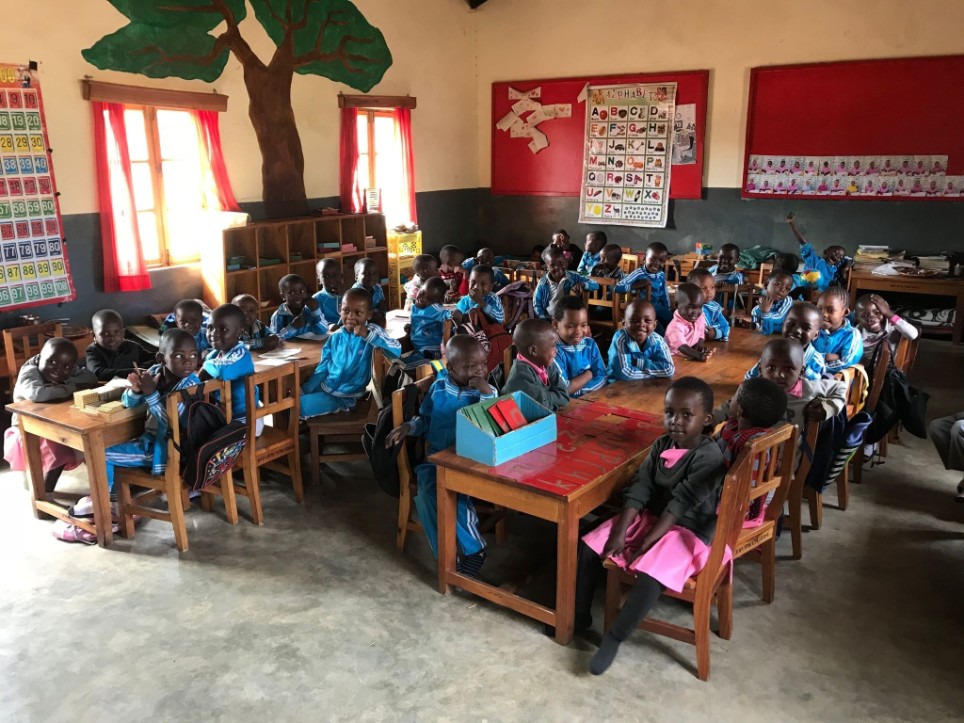 die Bayerische Spendenprojekt in Tansania Kleine Schülerinnen und Schüler sitzen in einem Klassenzimmer in Isele, Tansania und blicken freudig in die Kamera.