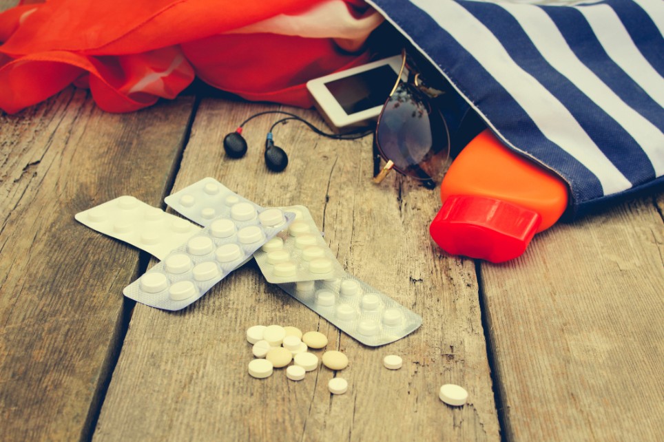 Verschiedene Medikamentenblister, die neben einer kleinen Reisetasche liegen Verschiedene Medikamentenblister, die neben einer kleinen Reisetasche liegen