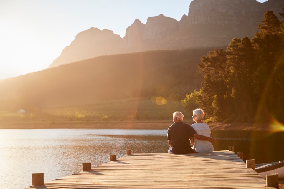 Ein älteres Ehepaar sitzt am Ende eines Stegs an einem See in den Bergen