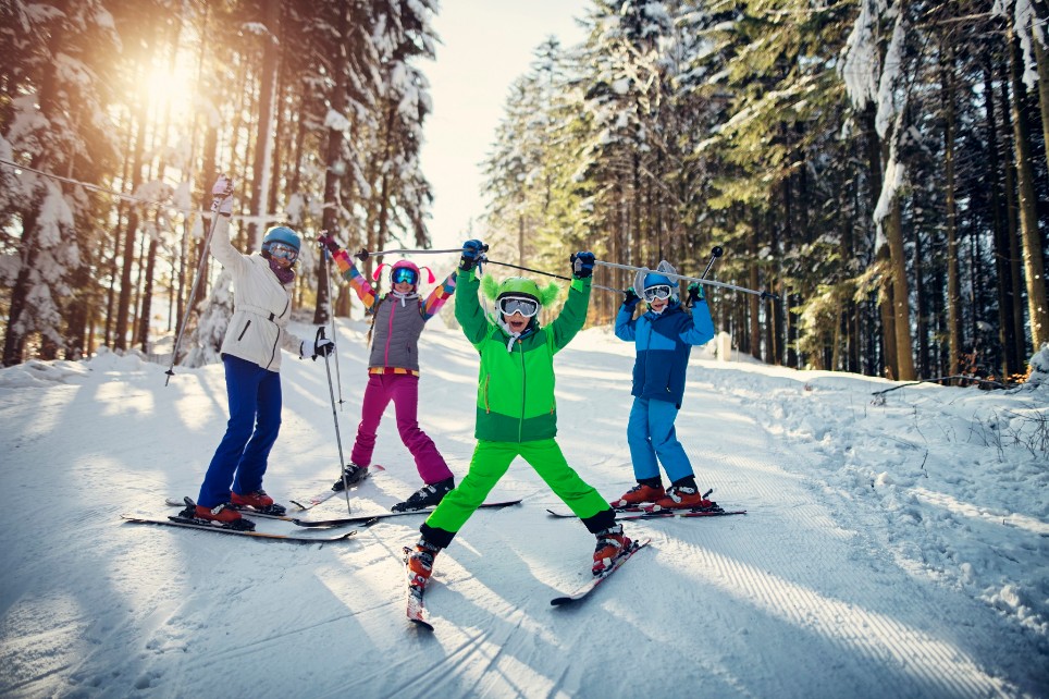 Mutter mit Kindern fährt gemeinsam die Skipiste hinunter. Alle lachen glücklich. Mutter mit Kindern fährt gemeinsam die Skipiste hinunter. Alle lachen glücklich.